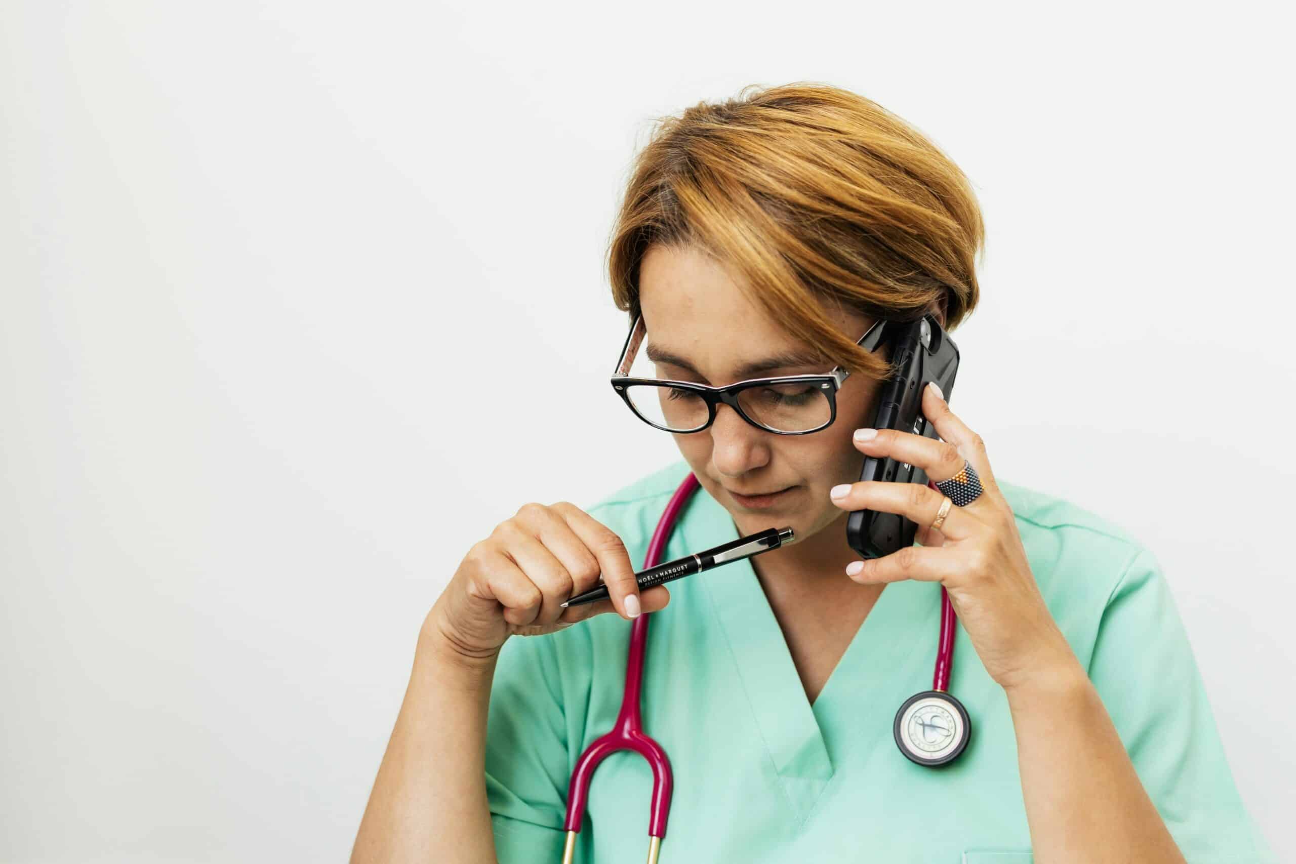 Focused female doctor with eyeglasses and stethoscope talking on the phone for medical consultation.