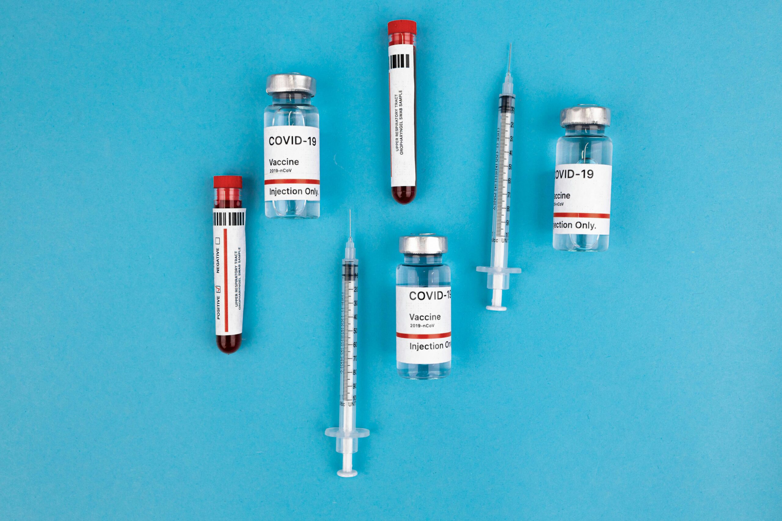 Top view of COVID-19 vaccine vials and syringes on a blue background, indicating medical research.