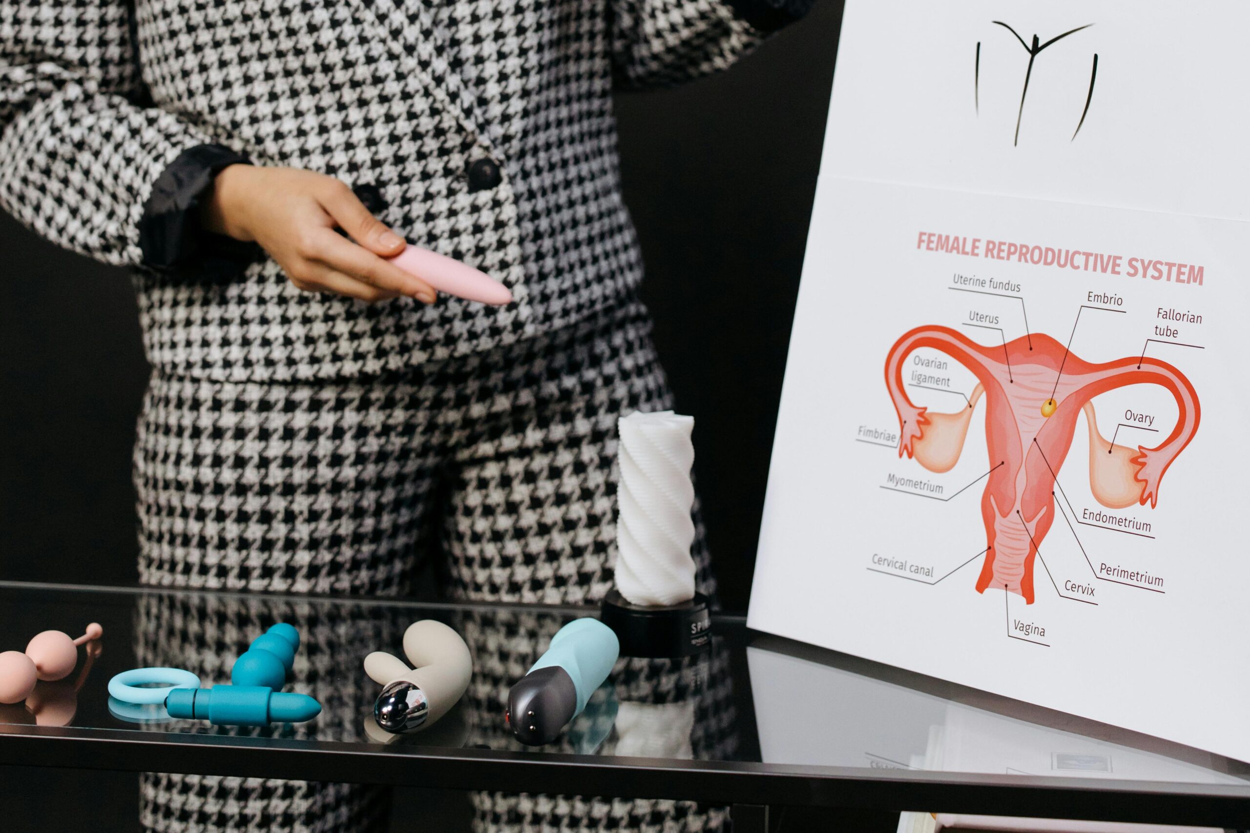 A person demonstrates various sex toys alongside a female reproductive system diagram, emphasizing education.